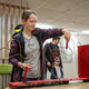 A woman tries to guide an iron ring along a wire without touching it. Another person can be seen in the background.