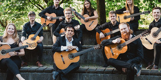 Ein Gruppenfoto des Gitarrenensembles. Die Zehn Musiker:innen halten ihre Gitarren auf dem Schoß.