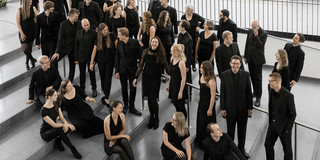Der Kammerchor der TU Dortmund Ein Gruppenfoto vom Kammerchor der TU Dortmund. Die schwarz gekleideten Musiker*innen sind von halboben fotografiert.