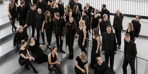 Ein Gruppenfoto vom Kammerchor der TU Dortmund. Die schwarz gekleideten Musiker*innen sind von halboben fotografiert.