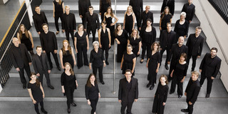 Ein Gruppenfoto vom Kammerchor der TU Dortmund. Die schwarz gekleideten Musiker*innen sind von oben fotografiert.
