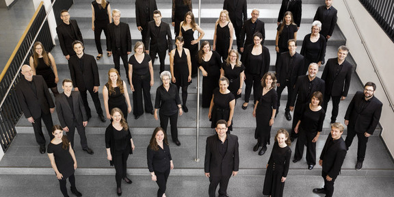 Ein Gruppenfoto vom Kammerchor der TU Dortmund. Die schwarz gekleideten Musiker*innen sind von oben fotografiert.