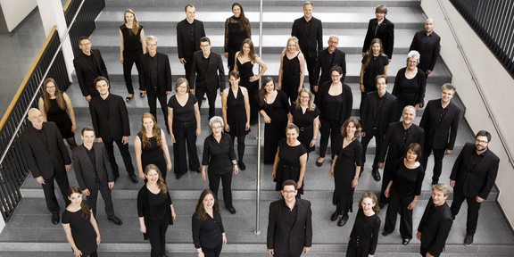Ein Gruppenfoto vom Kammerchor der TU Dortmund. Die schwarz gekleideten Musiker*innen sind von oben fotografiert.