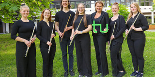 Gruppenbild des Ensembles "TU Flutes", die Musiker*innen halten ihre Flöten in der Hand, die Leiterin hält ein grünes TU-Logo in der Hand.