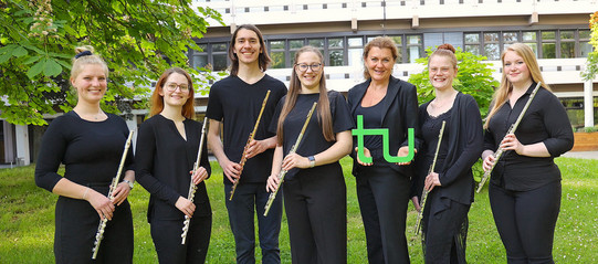 Gruppenbild des Ensembles "TU Flutes", die Musiker*innen halten ihre Flöten in der Hand, die Leiterin hält ein grünes TU-Logo in der Hand.