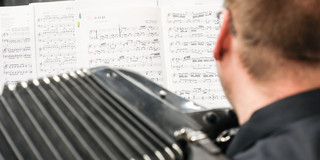 Maik Hester spielt Akkordeon, Fokus der Kamera liegt auf den Notenblättern, die er liest.